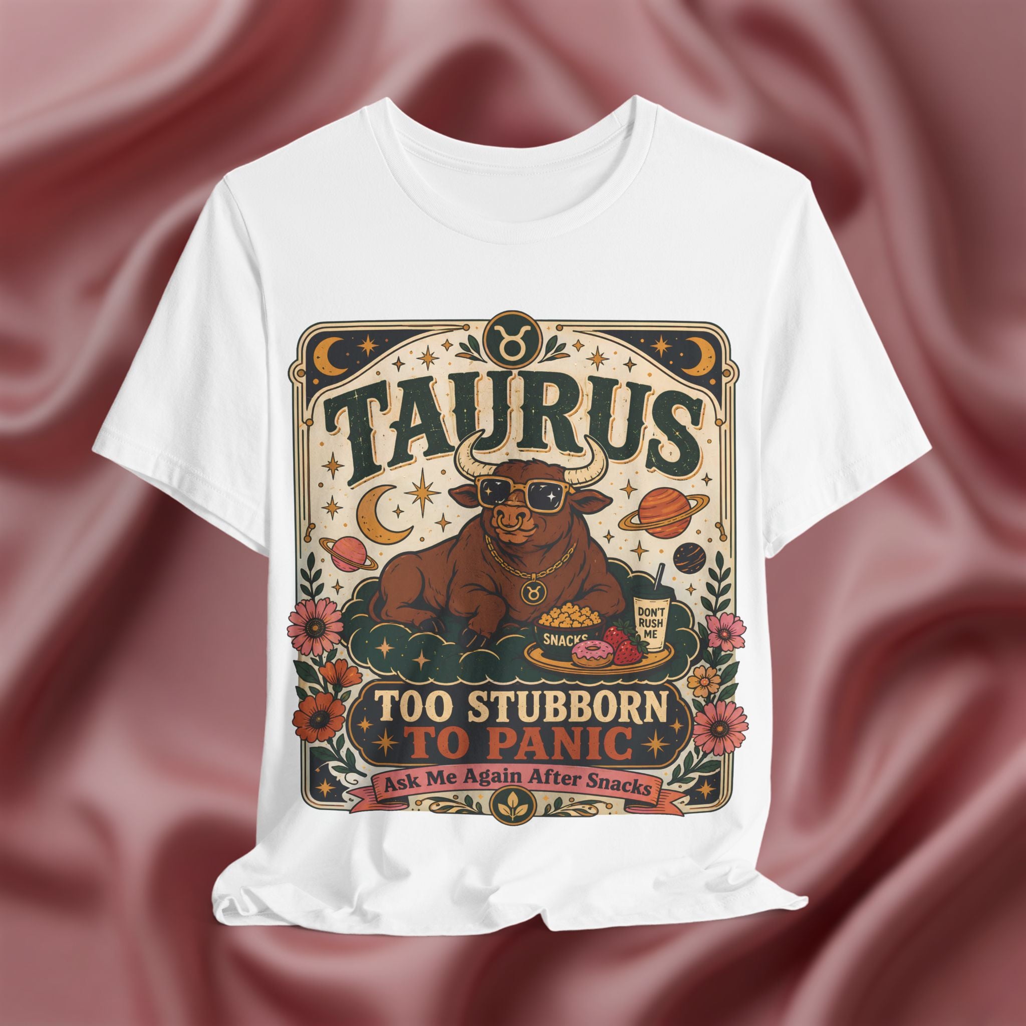 White t-shirt with Taurus zodiac design on a maroon fabric background