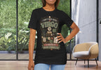 A woman modeling a black graphic t-shirt with a vintage-style 'Virgo' design, standing in a modern room with large windows and a chair.