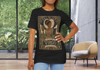 A woman modeling a black graphic t-shirt with a vintage-style 'The Maiden Virgo' celestial print, standing in a modern room with large windows and a beige armchair.