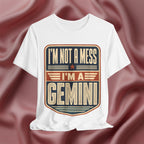 White t-shirt with 'I'm not a mess, I'm a Gemini' design on a pink fabric background
