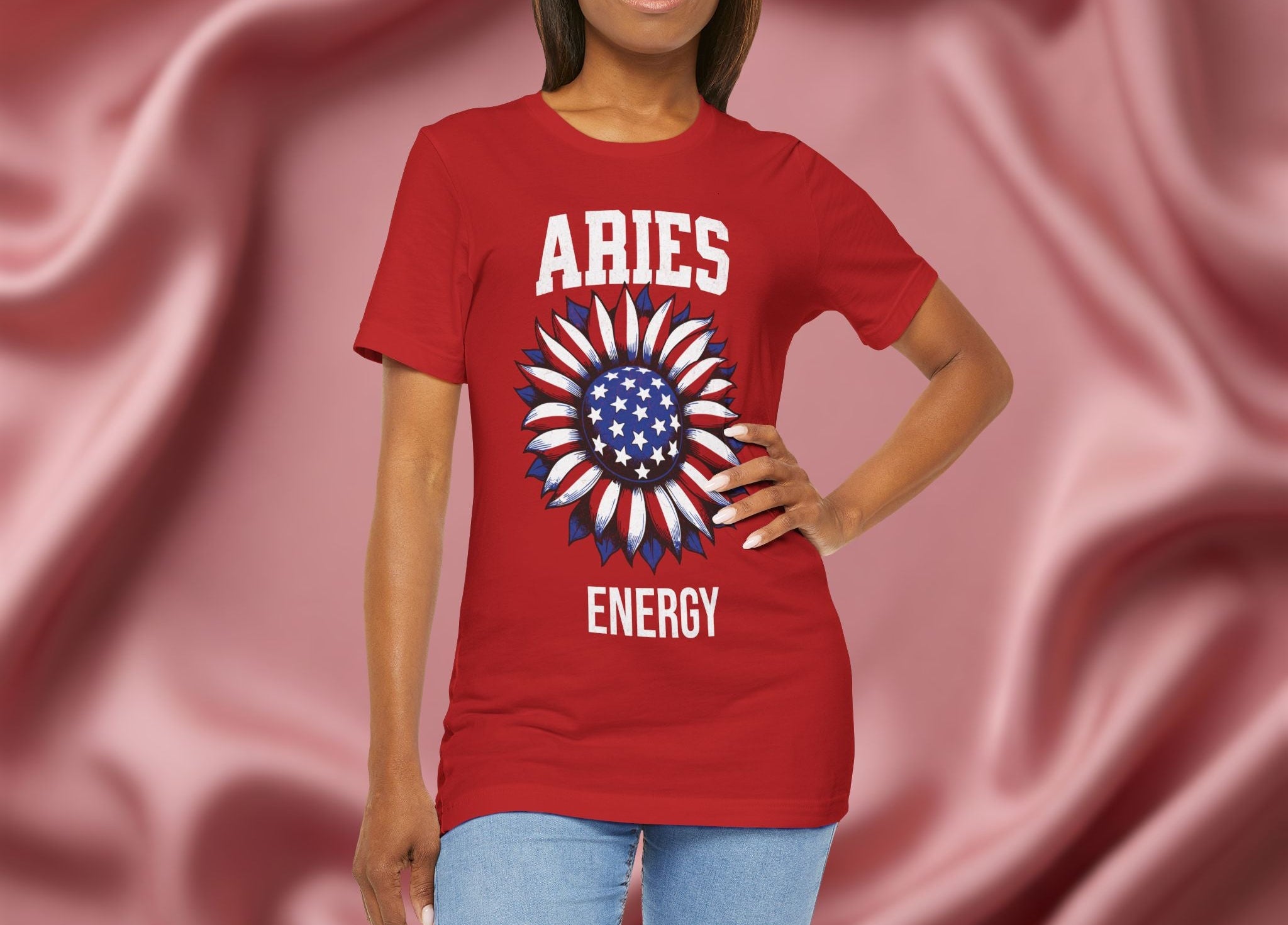 Woman wearing a red t-shirt with American flag sunflower and 'ARIES ENERGY' text on a textured pink background