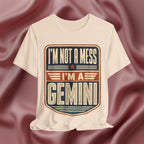 Soft cream with 'I'm not a mess, I'm a Gemini' design on a maroon fabric background