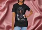 Woman wearing a black t-shirt with a graphic design of a woman, flowers, and the word 'Gemini' on a pink fabric background.