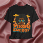 A black short-sleeve graphic T-shirt displayed against a draped dusty rose satin fabric background. The graphic features a retro-style illustration of a woman with an afro, sunglasses, and clouds, with the text 'VIRGO ENERGY' in orange and teal.