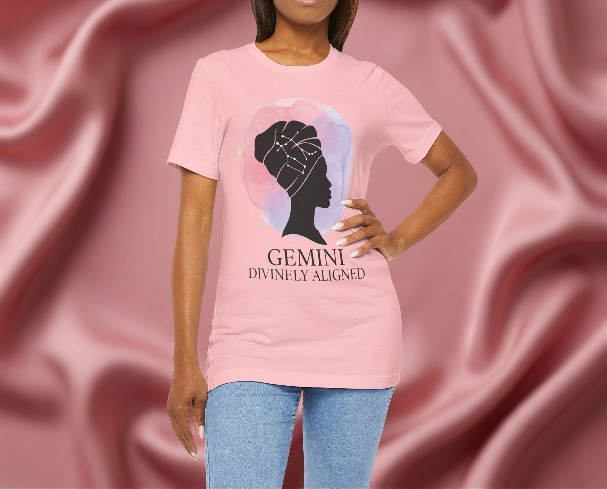 Woman wearing a pink t-shirt with a silhouette of a woman and 'Gemini Divinely Aligned' text on a pink fabric background