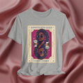 Sophisticated Queen Gemini Energy Gray t-shirt with a graphic design of a woman holding coffee cups on a pink fabric background