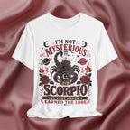 White t-shirt with Scorpio zodiac design and text on a maroon fabric background