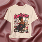 Soft cream t-shirt with Capricorn zodiac design featuring a woman and goat on a maroon fabric background.